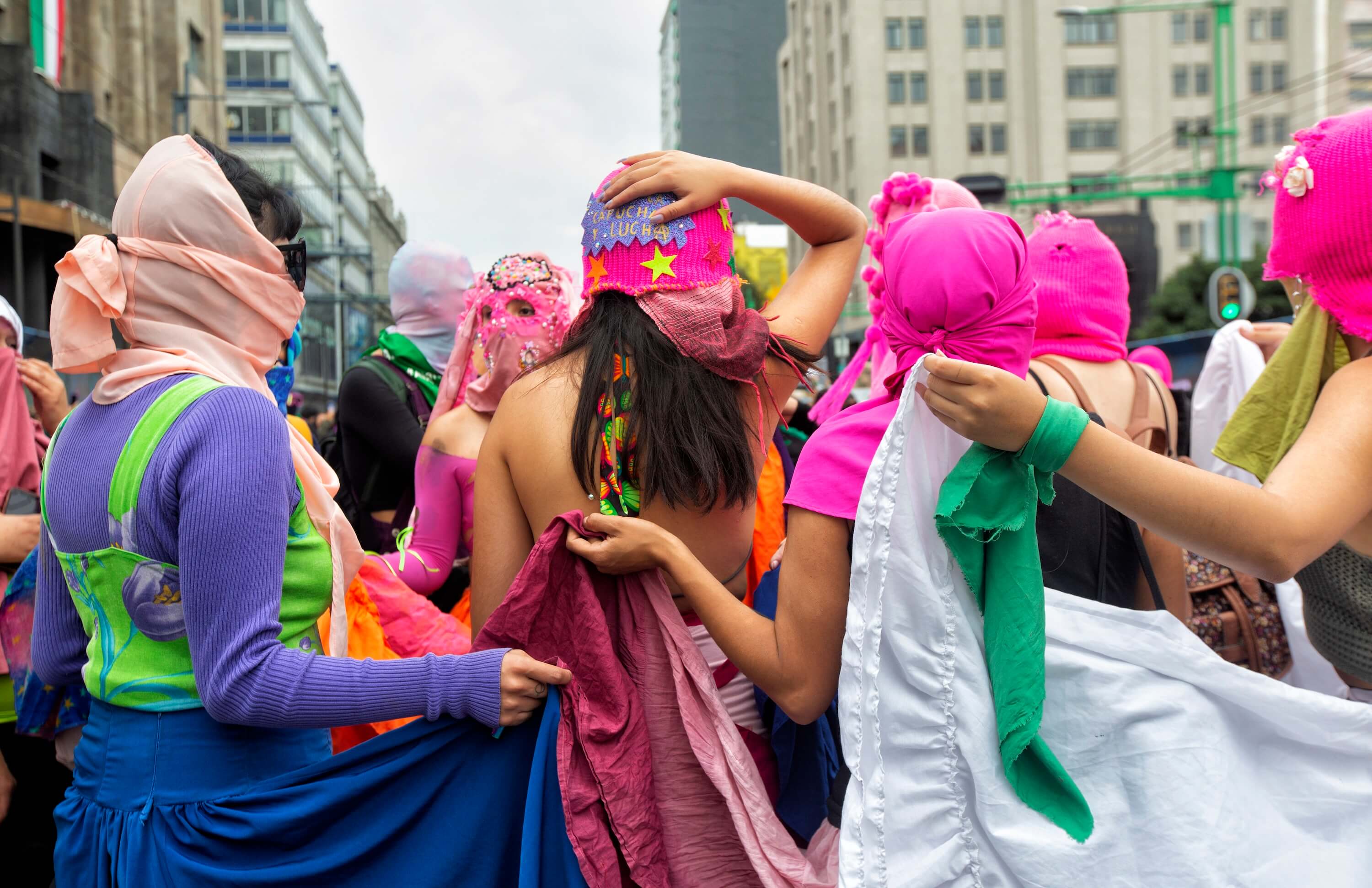 Fotografía en plano medio de varias mujeres que conforman el colectivo "Capuchas rosas". Usan pasamontañas color rosa y faldas de folklore mexicano.