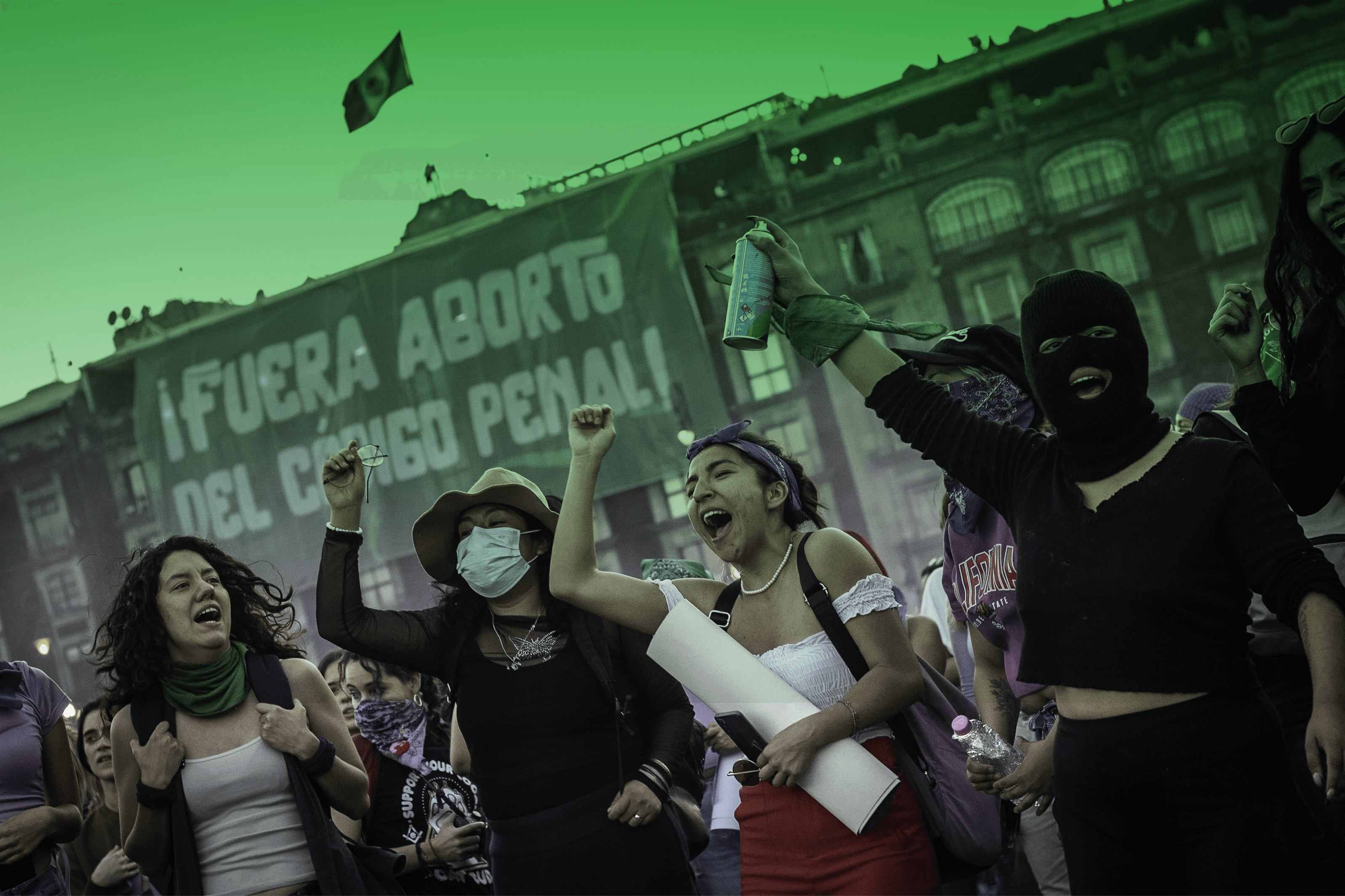 Fotografía en plano medio de varias personas que se encuentran frente a un edificio del Centro Histórico de la CDMX. Están en una manifestación gritando y alzando el puño derecho.