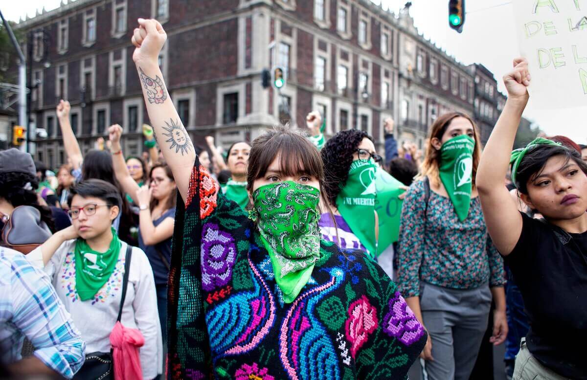 Fotografía en plano medio de un grupo de mujeres en una manifestación. Cuatro de ellas usan pañuelos aborteros cubriendo sus rostros.